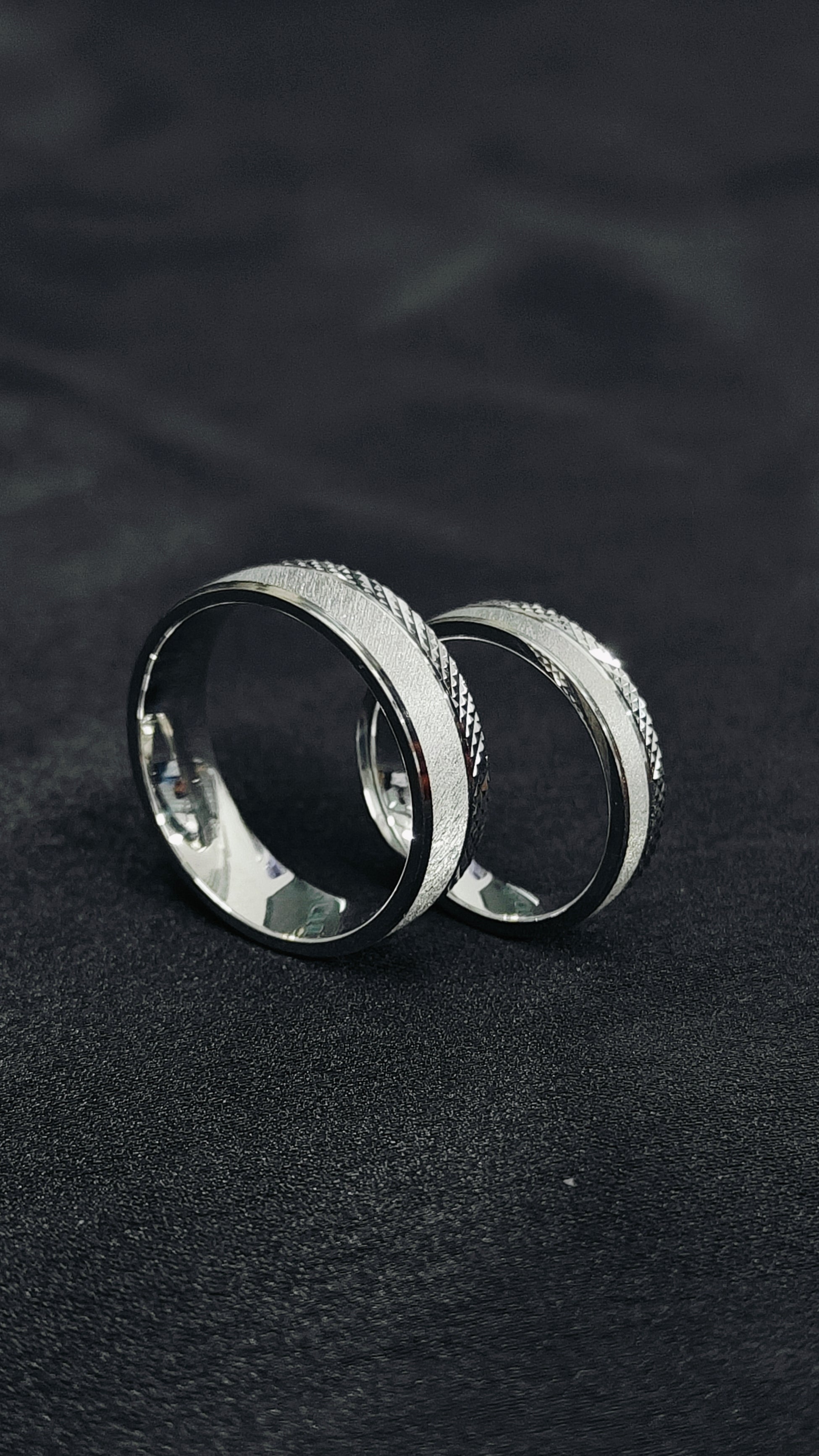 Two silver rings with textured surfaces on a dark fabric background