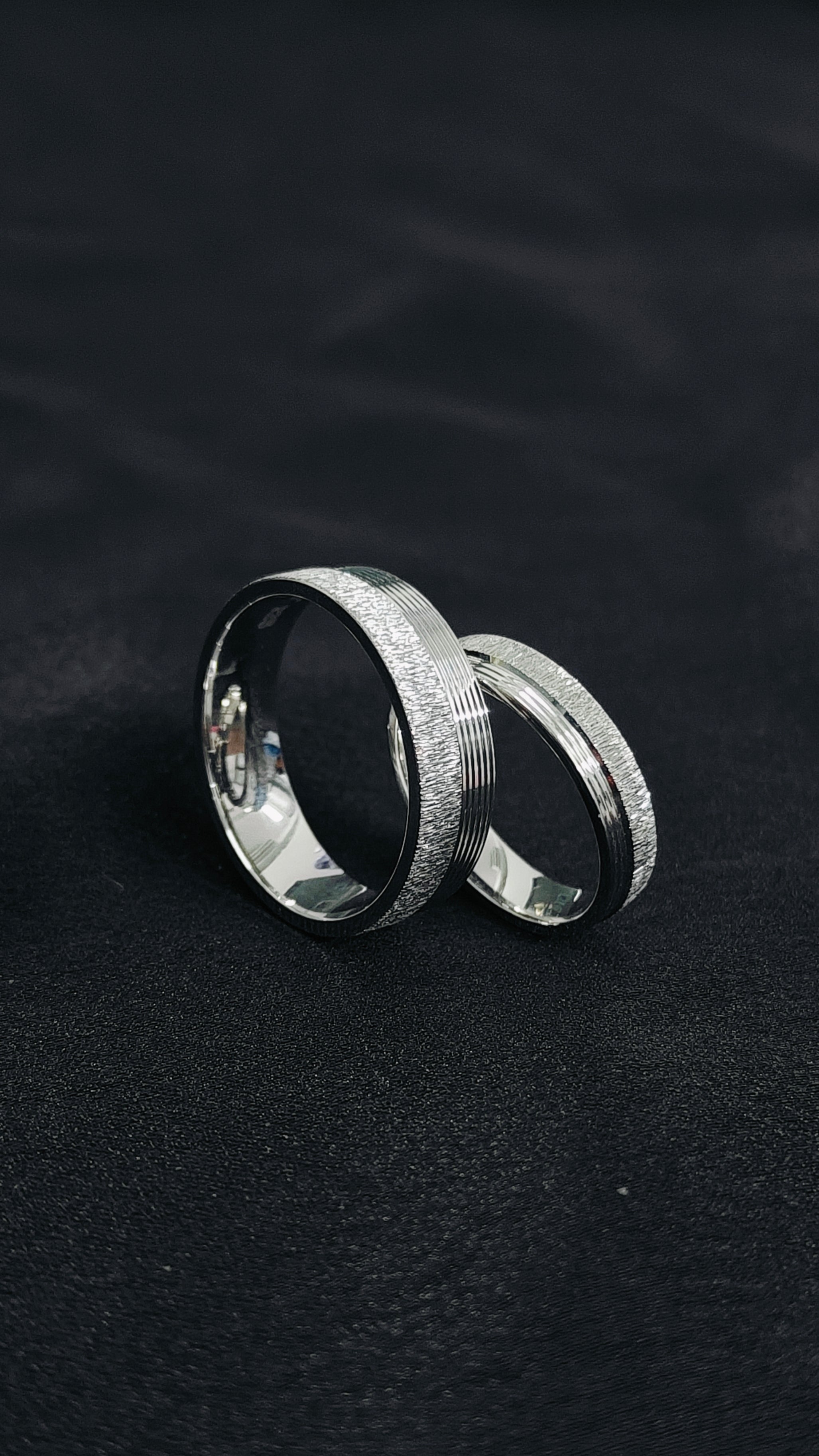 Two silver rings on a black textured surface