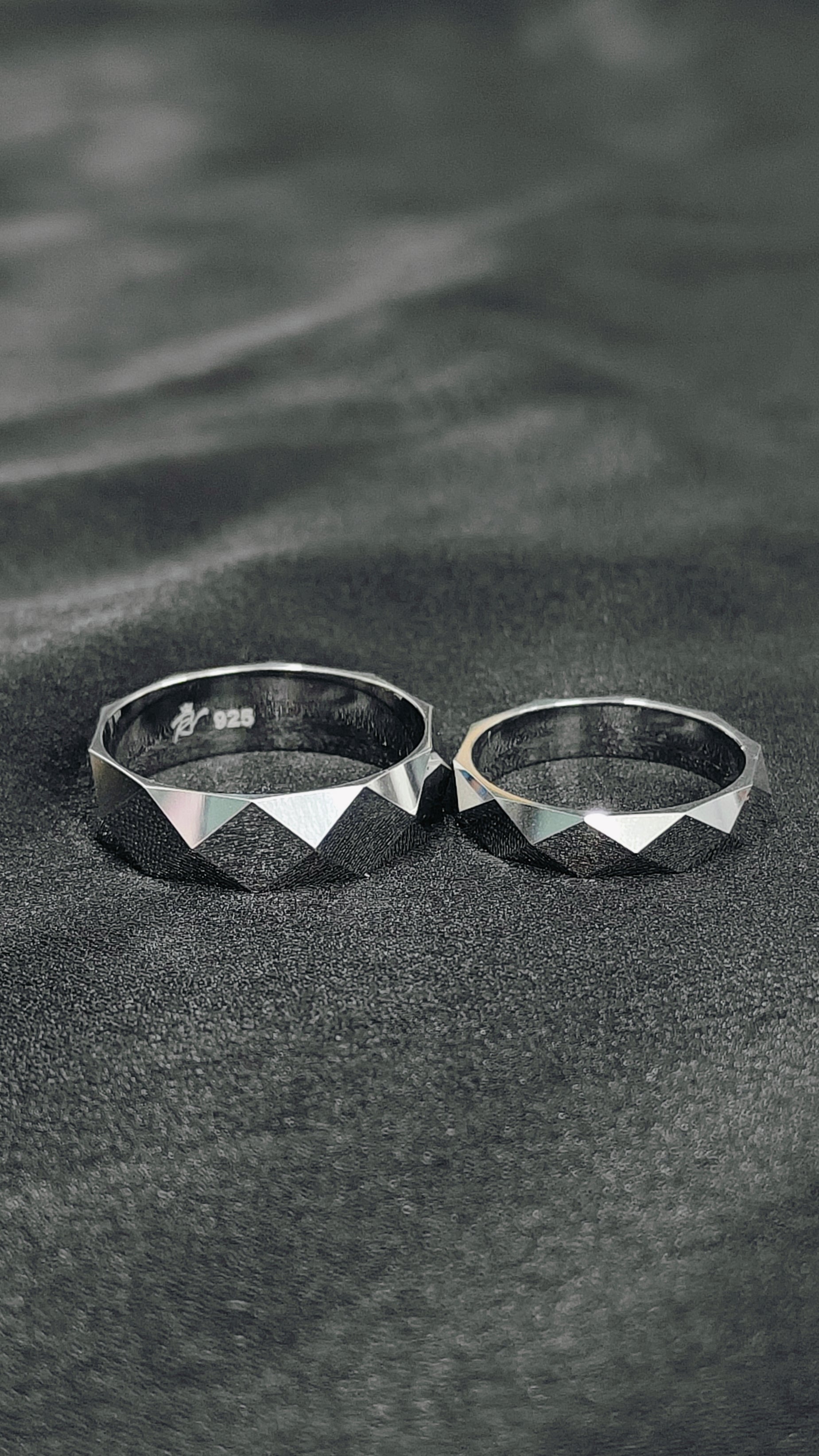 Two silver rings with geometric designs on a textured surface