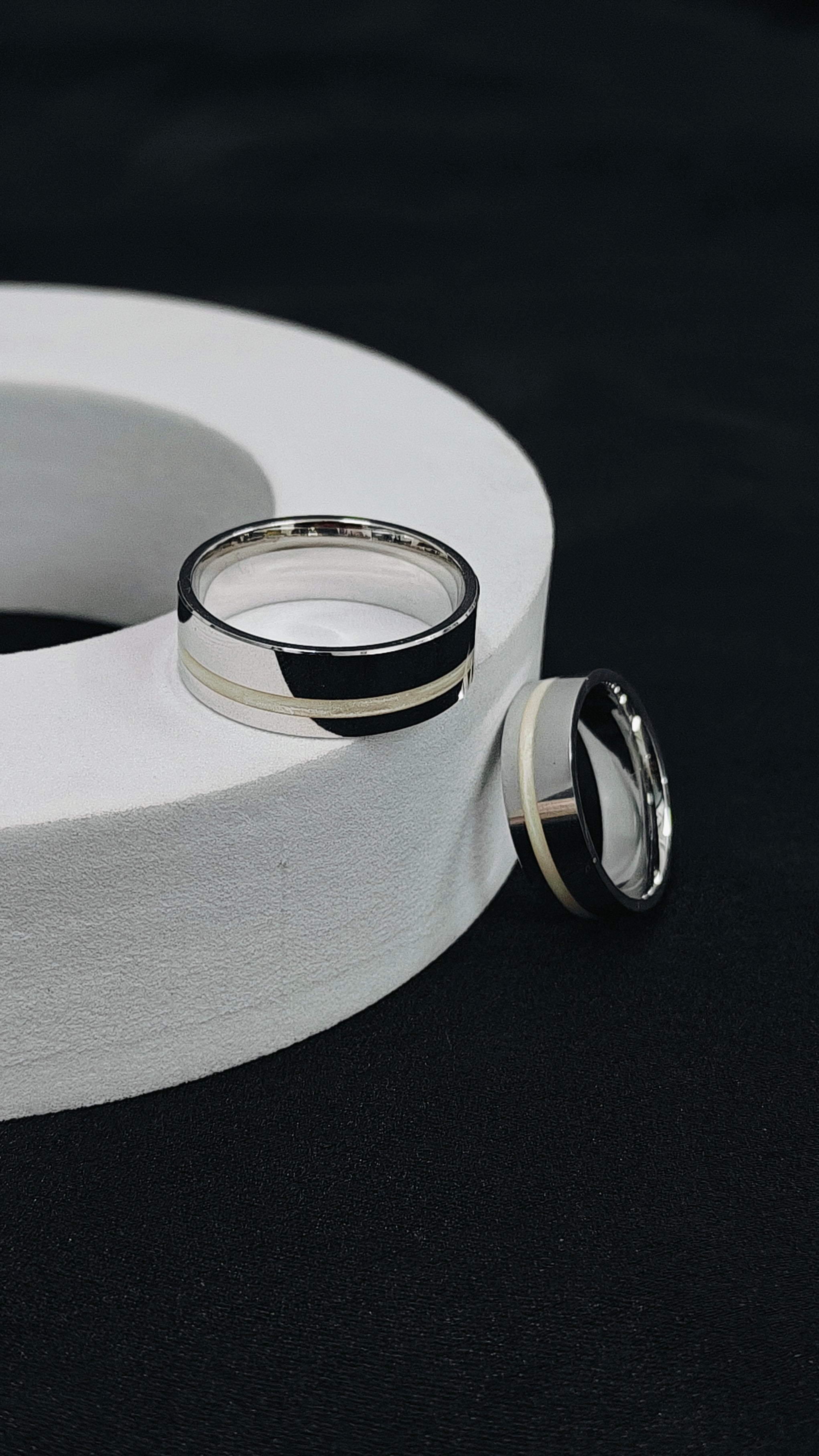 Two silver rings on a white circular stand against a black background