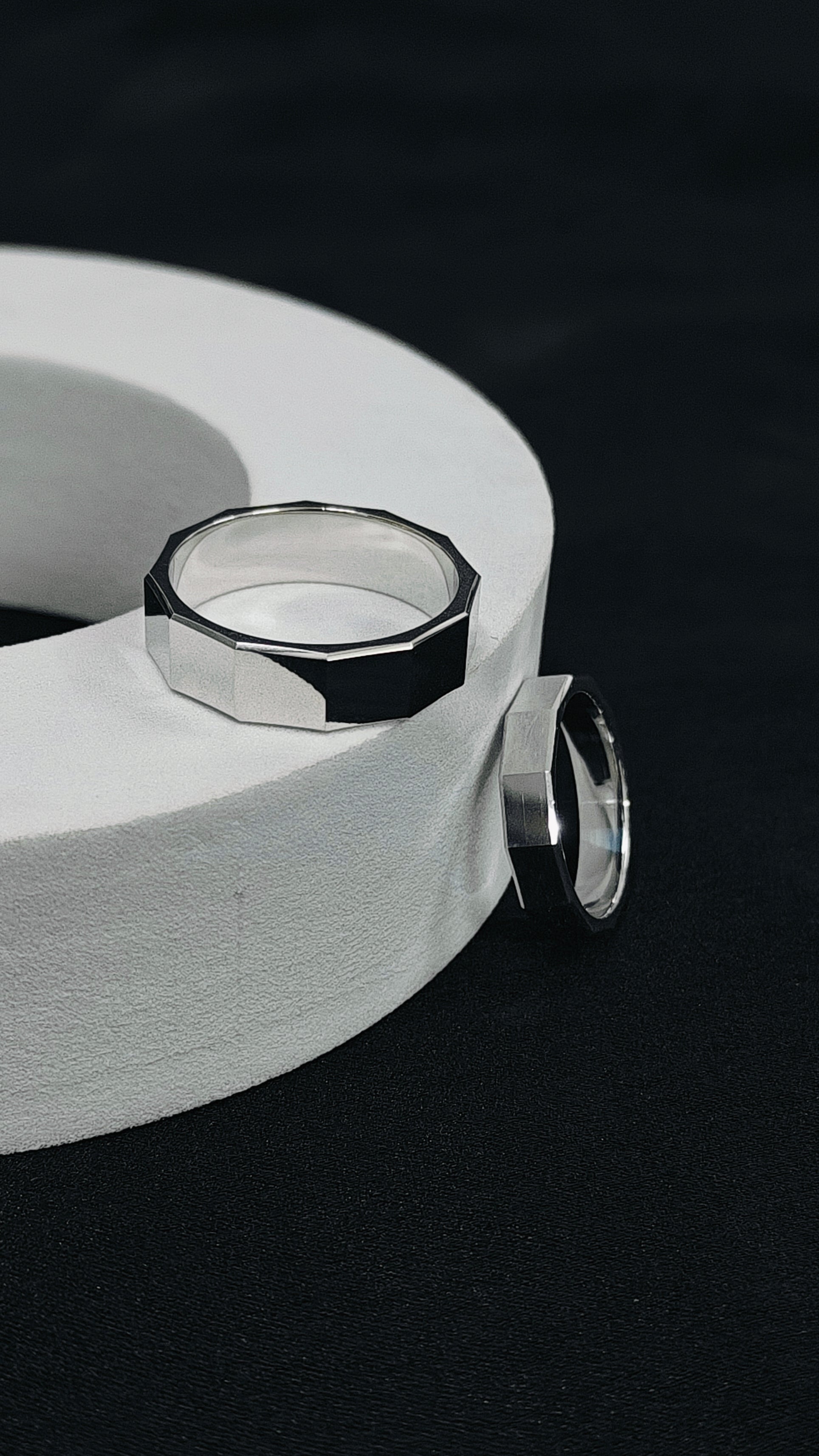 Silver ring with geometric design on a white cylindrical object against a black background