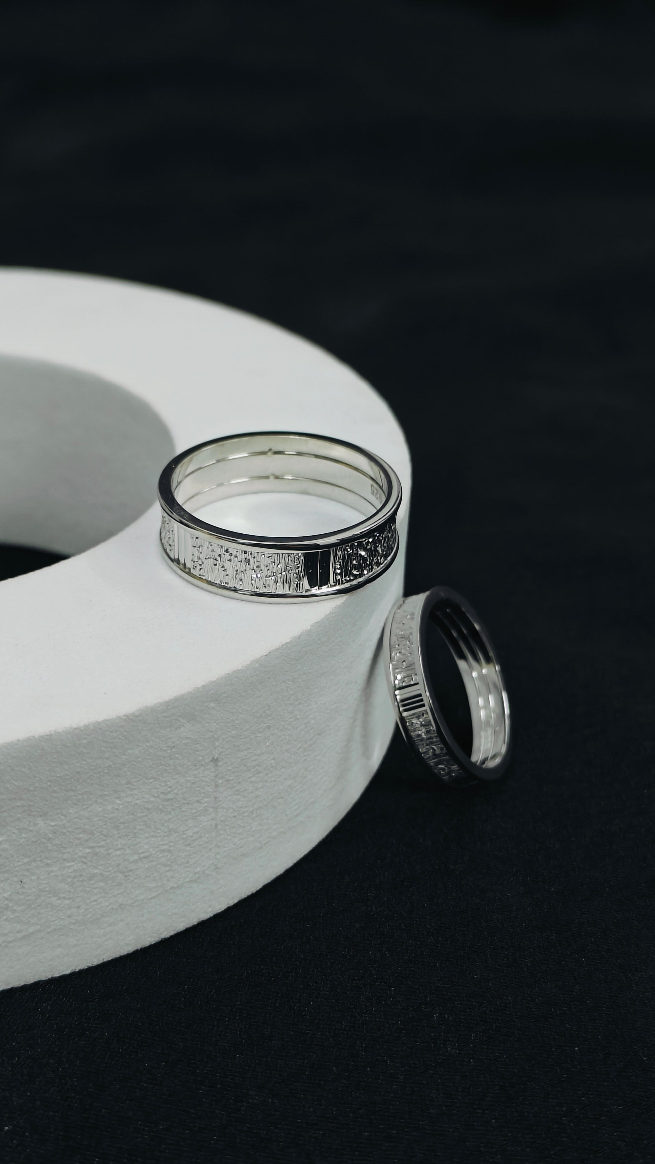 Two silver rings on a white cylindrical object against a black background