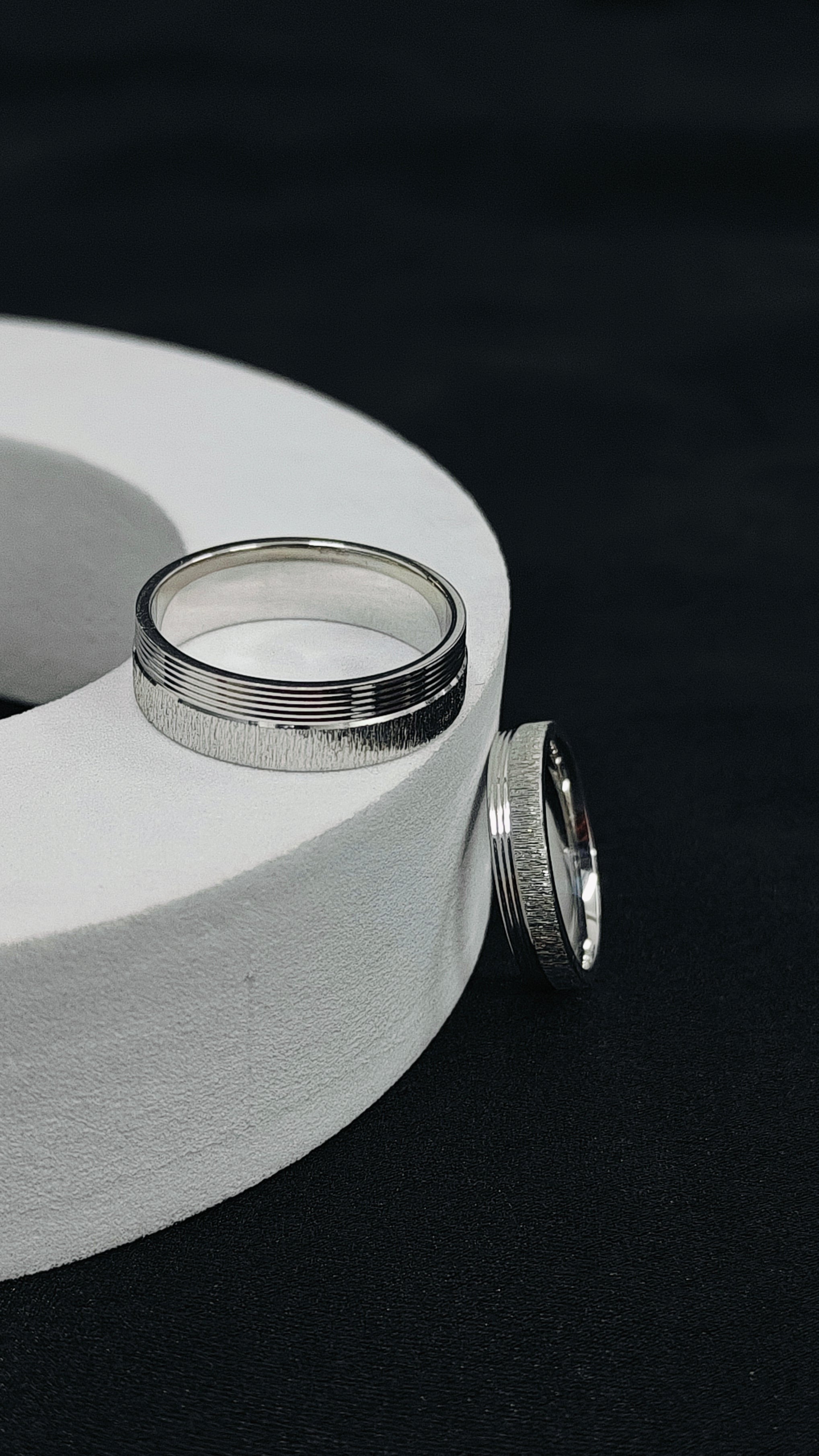 Two silver rings on a white circular stand against a black background