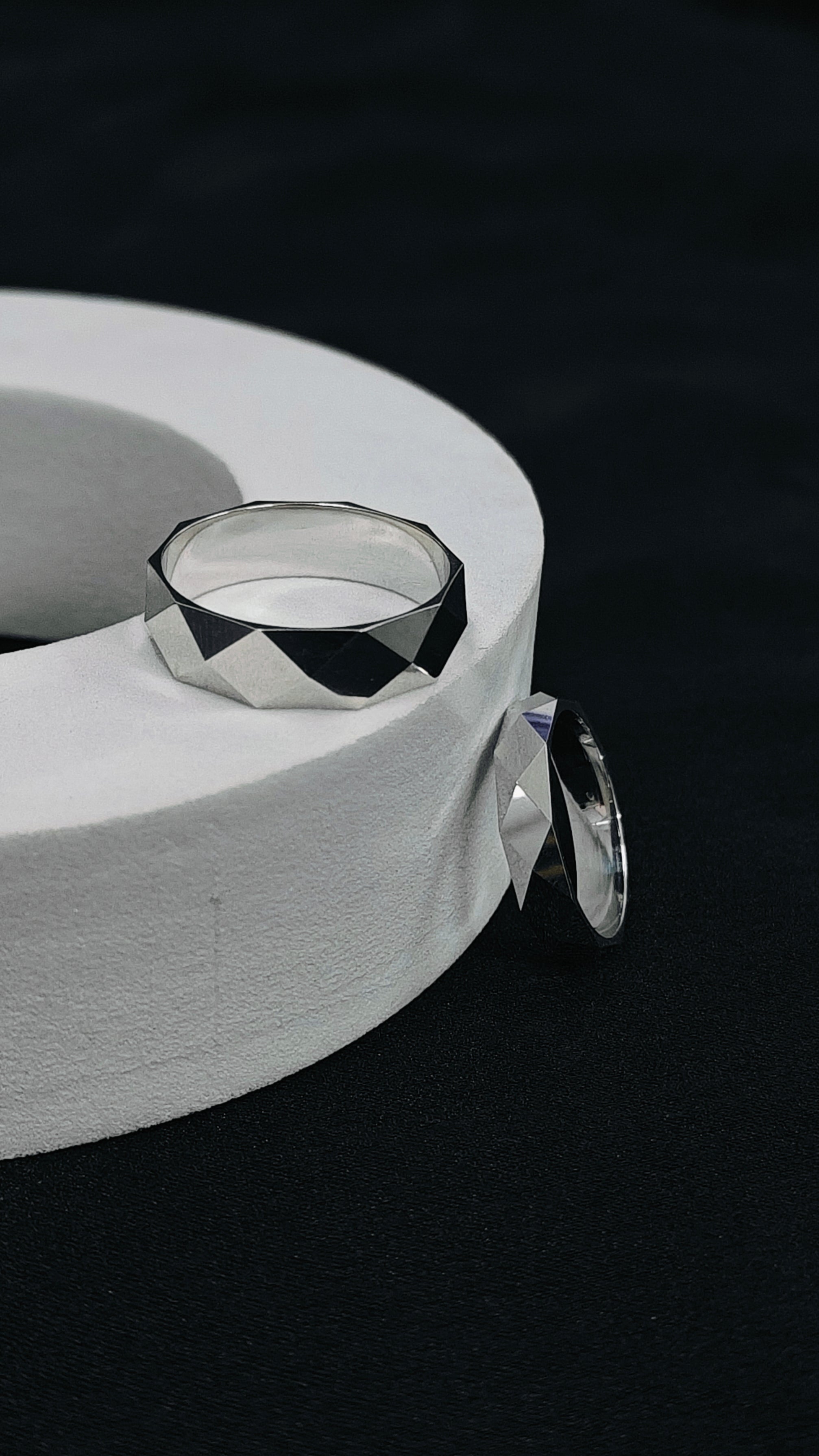 Silver ring on a white cylindrical stand against a black background