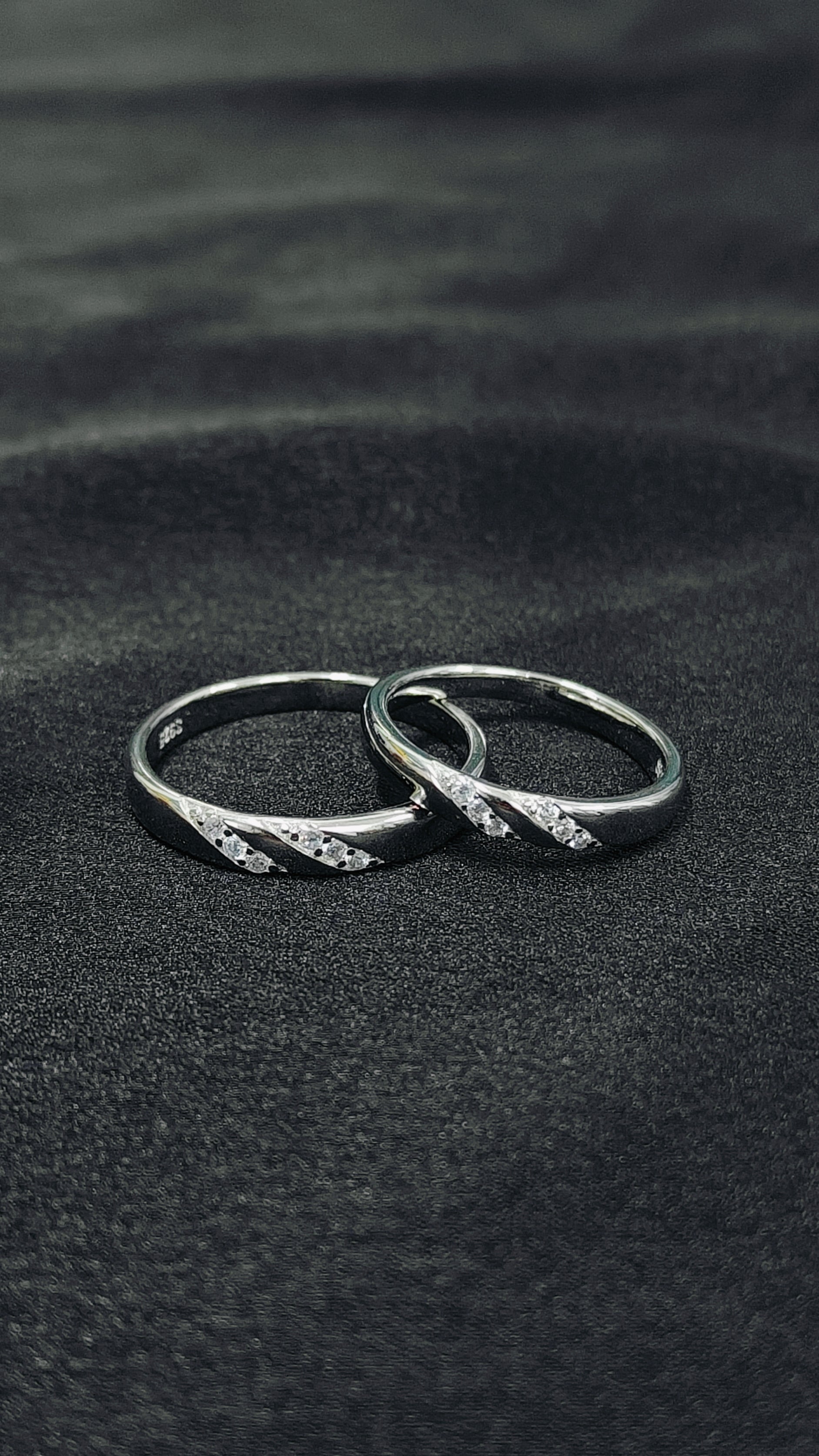 Two silver rings with small diamonds on a black sand background