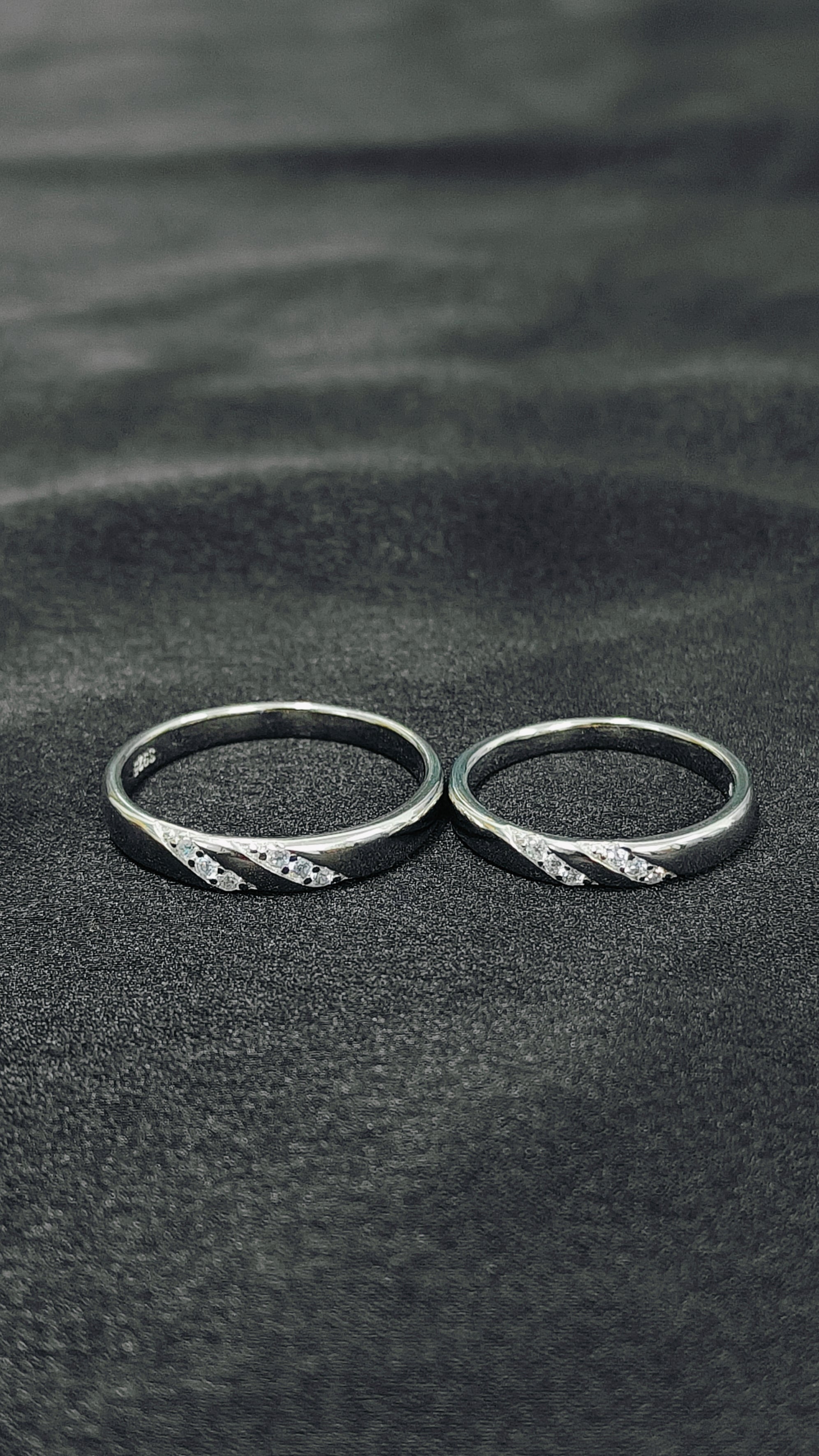 Two silver rings with textured band design on a dark sand background