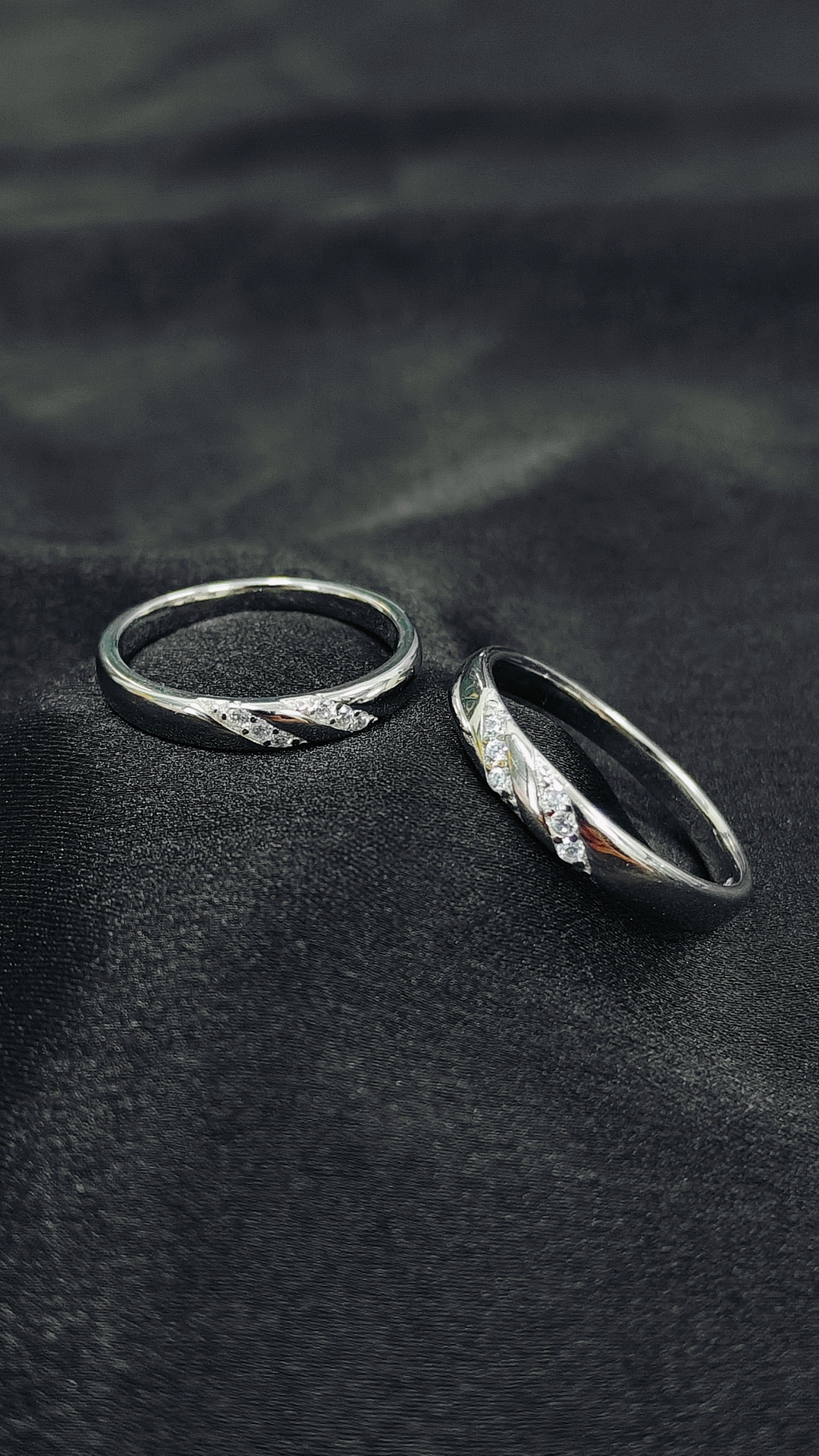 Two silver rings with intricate designs on a dark fabric background