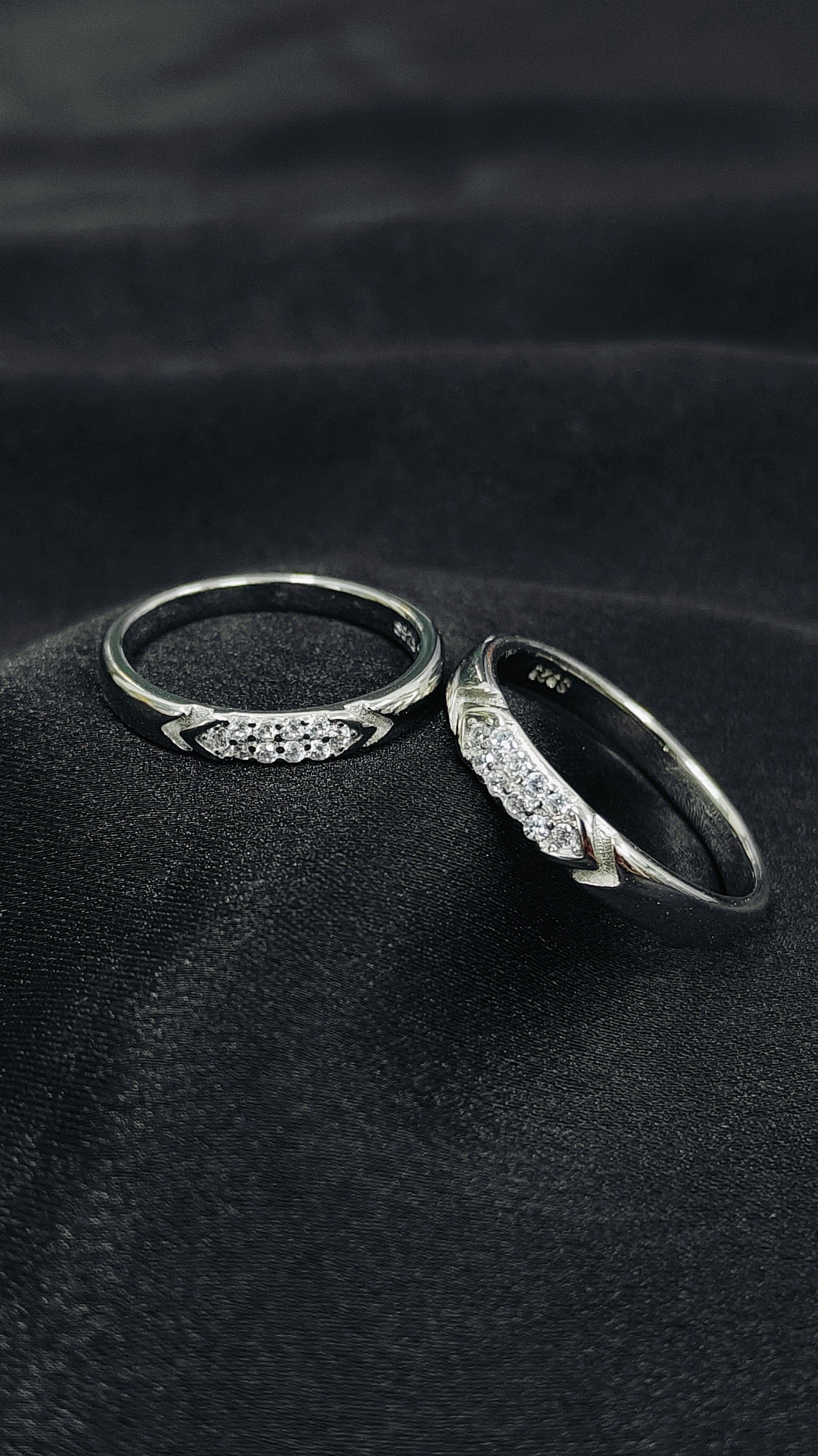 Two silver rings with intricate designs on a dark fabric background