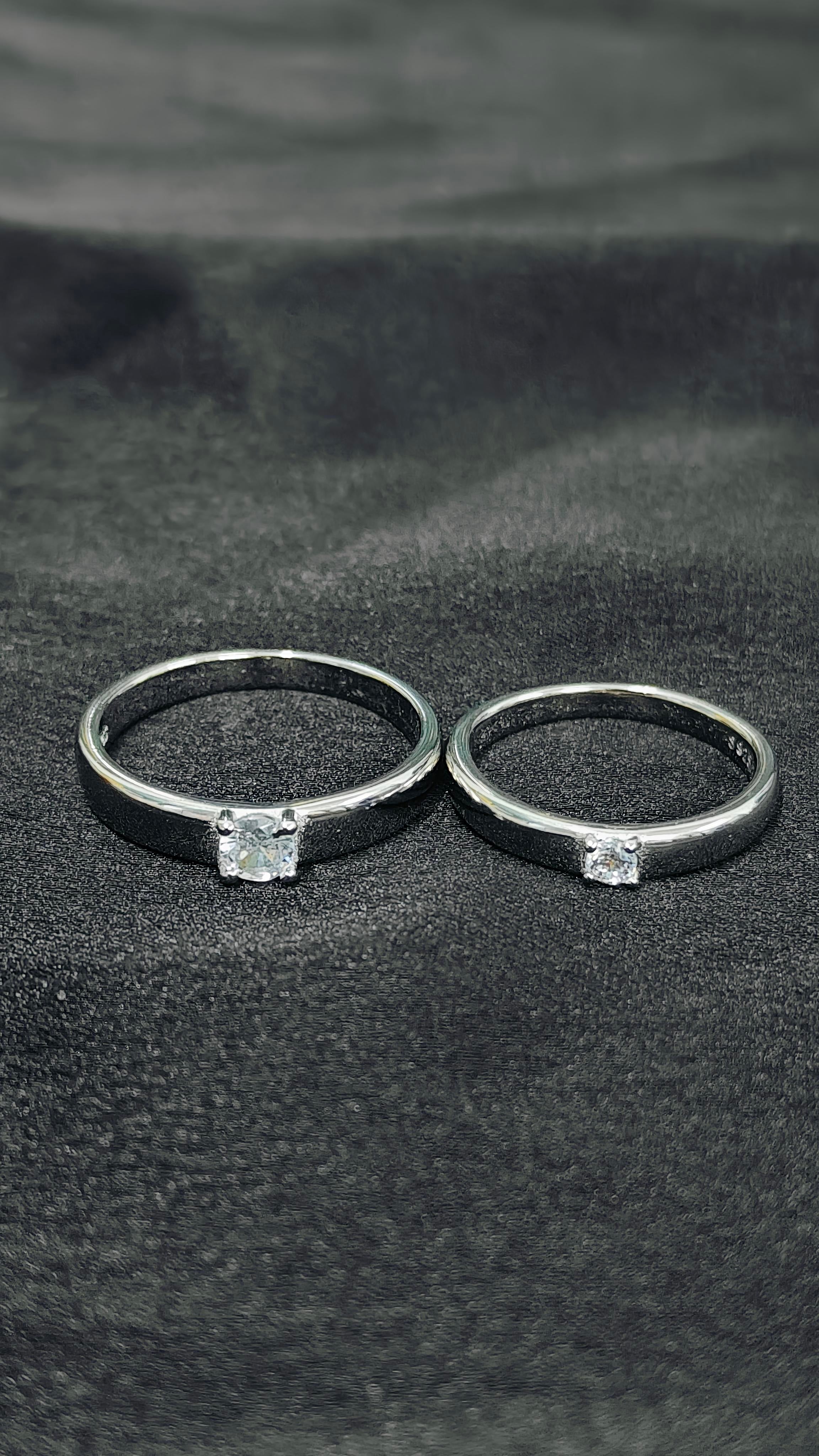 Two blackened silver rings with embedded diamonds on a dark fabric background