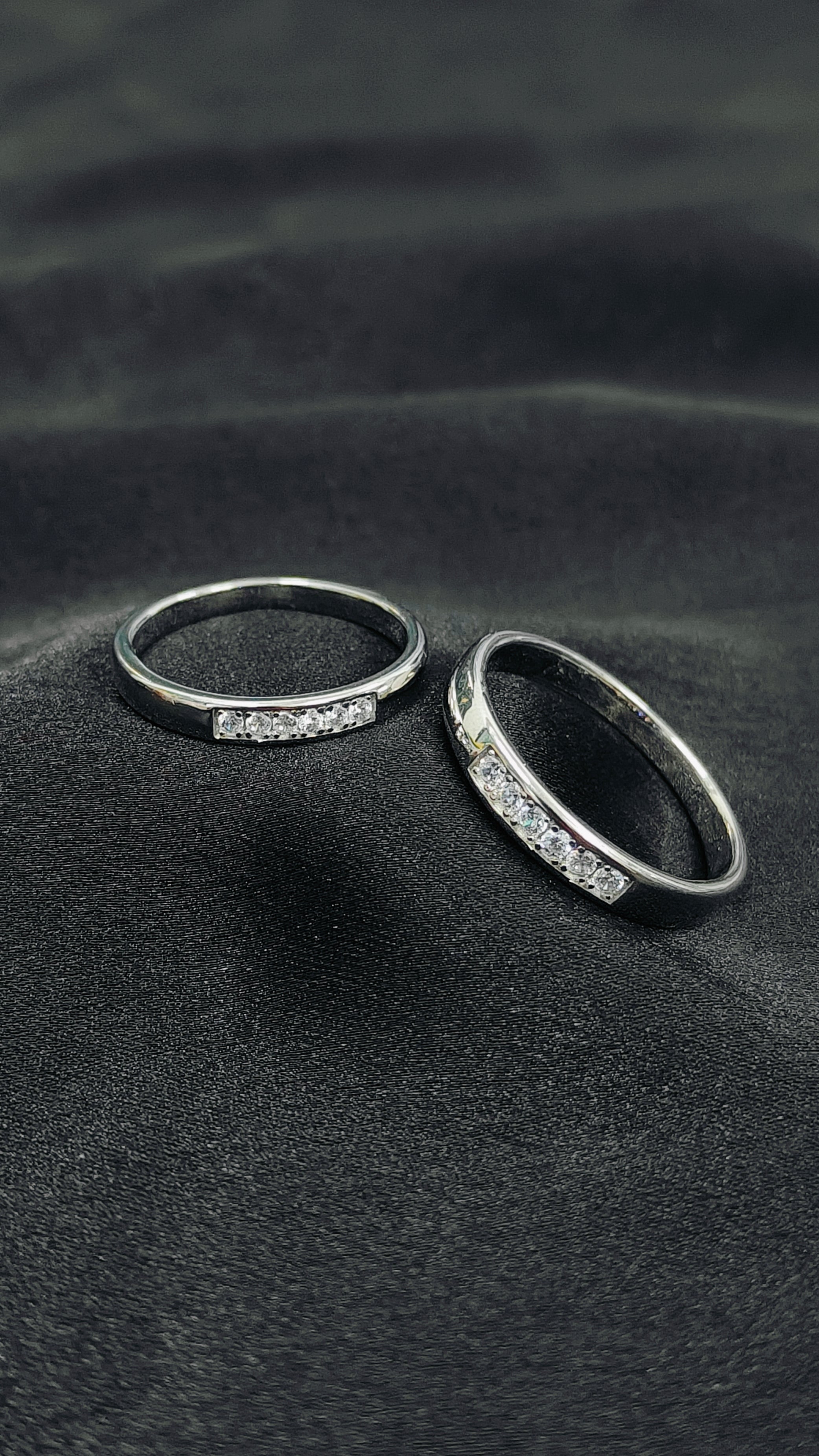 Two silver rings with embedded stones on a dark textured surface