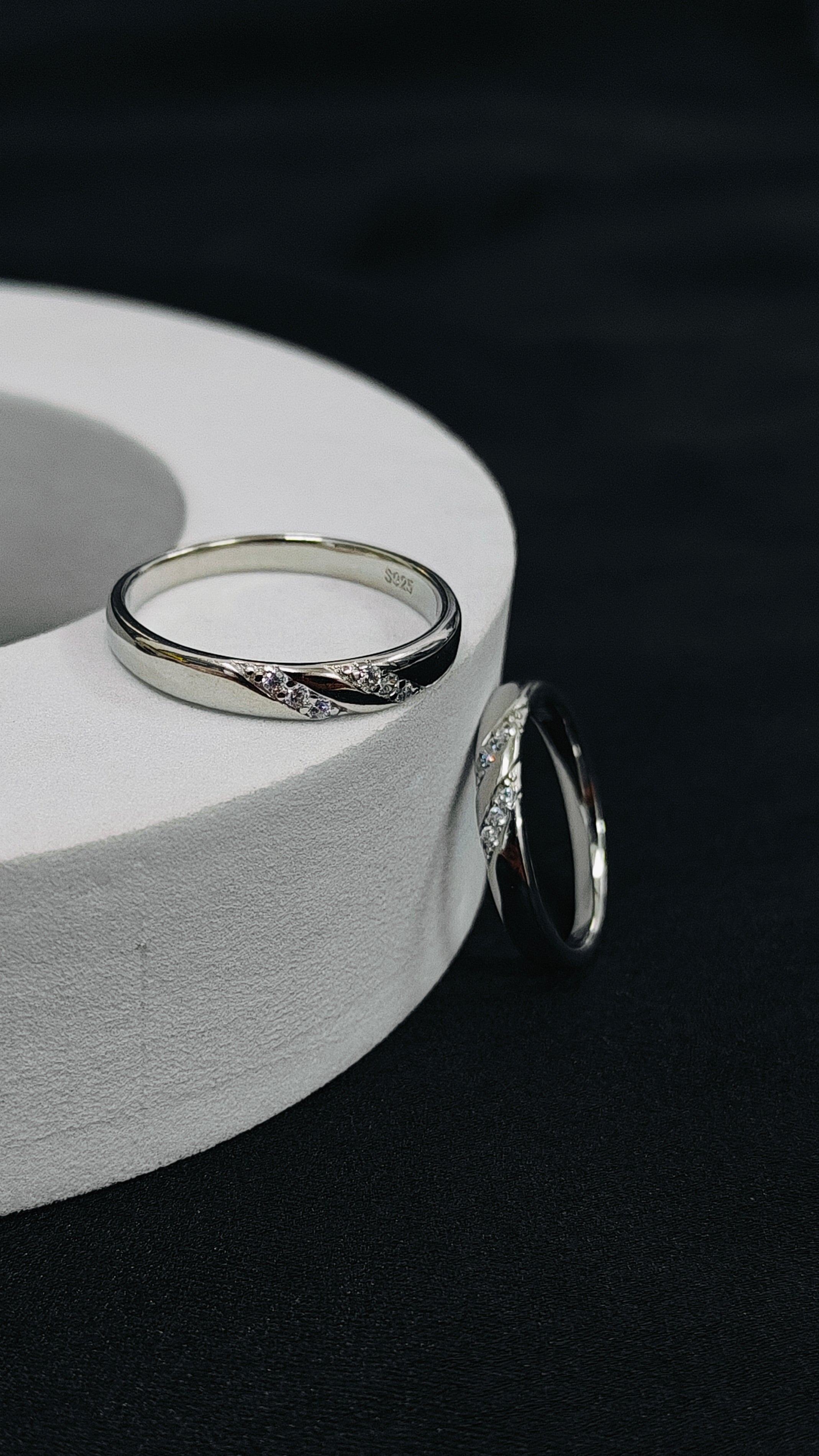 Two silver rings on a white cylindrical stand against a black background