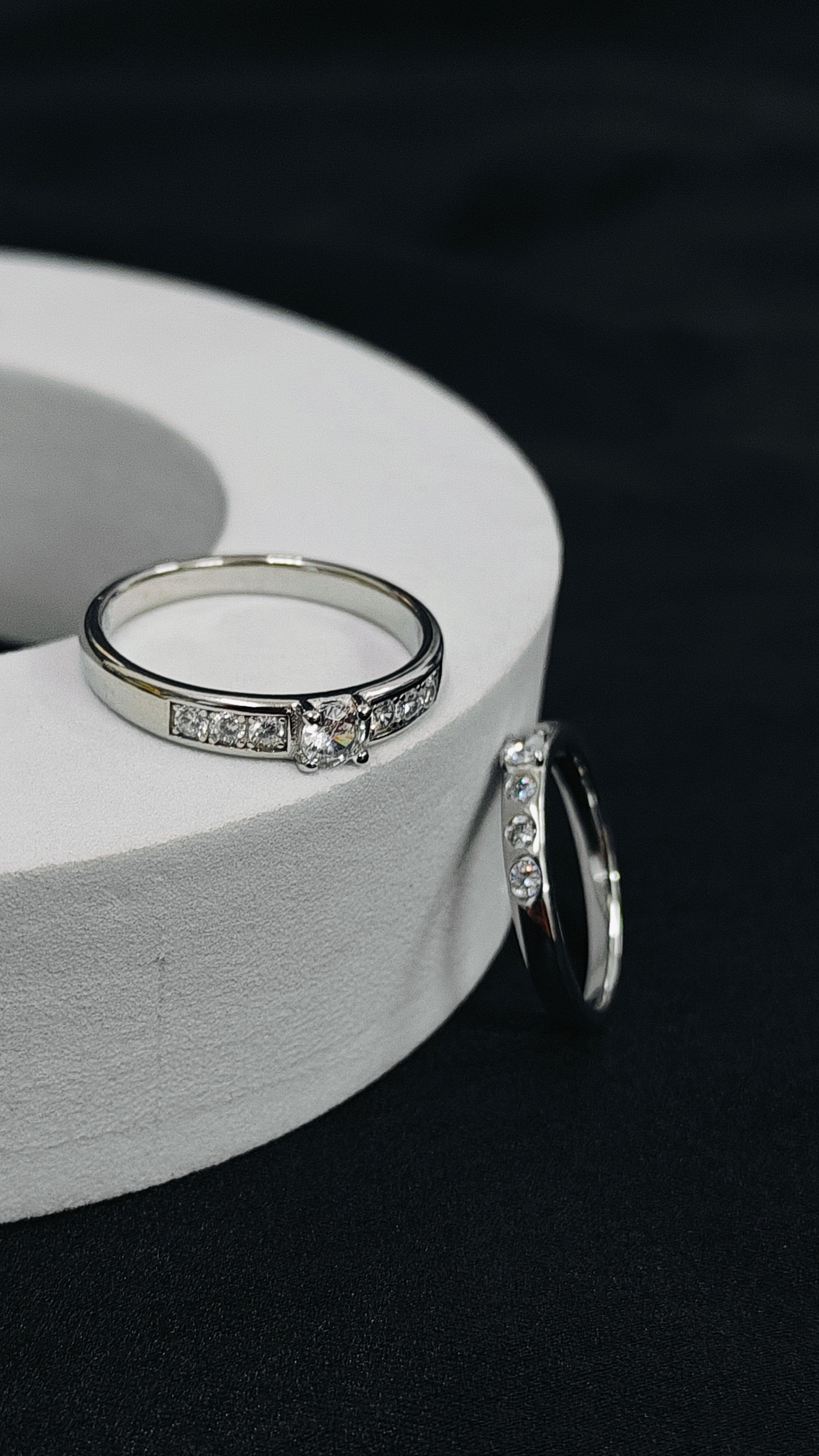 Silver ring with embedded diamonds on a white cylindrical object against a dark background
