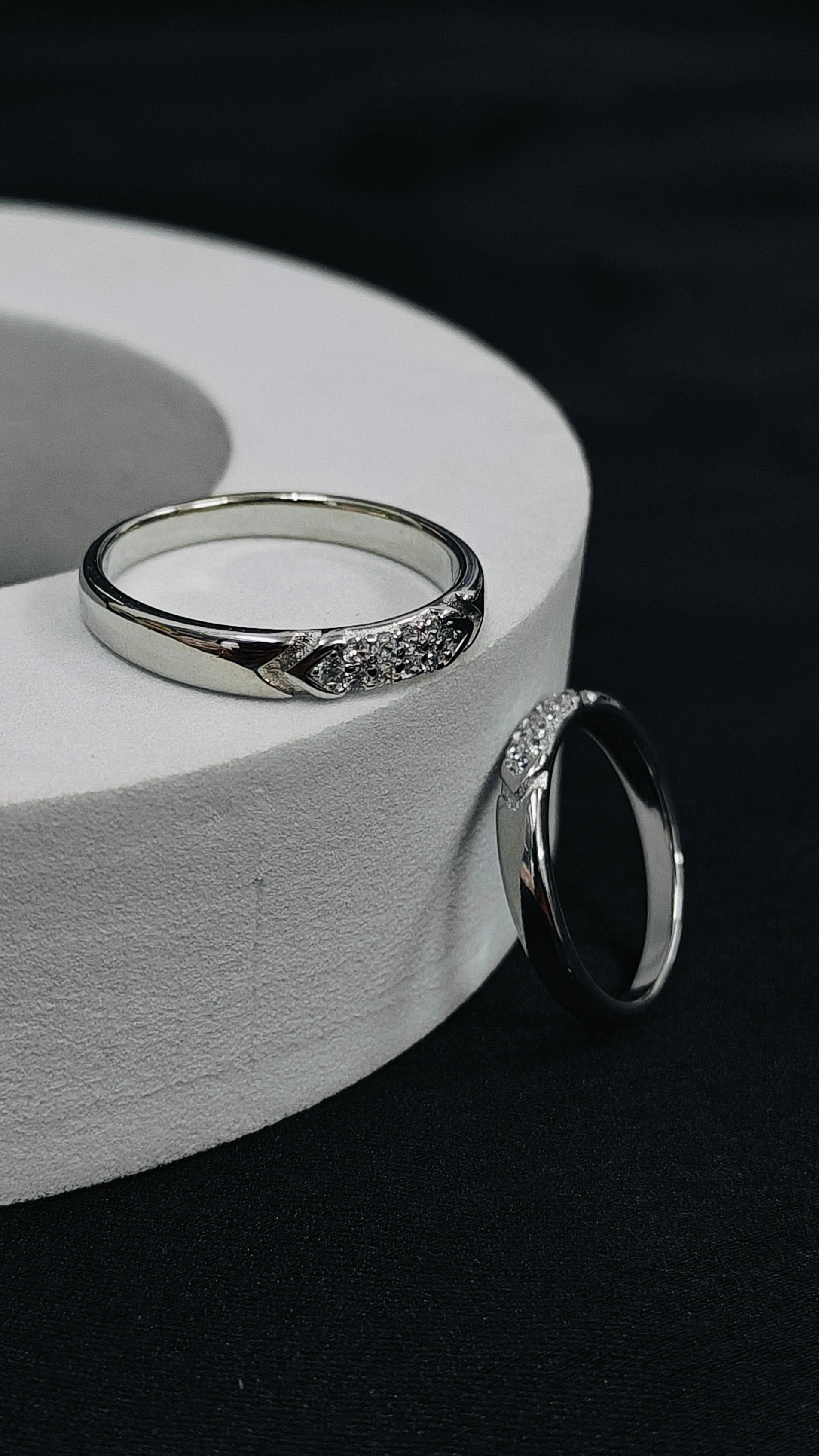 Two silver rings on a white cylindrical stand against a dark background