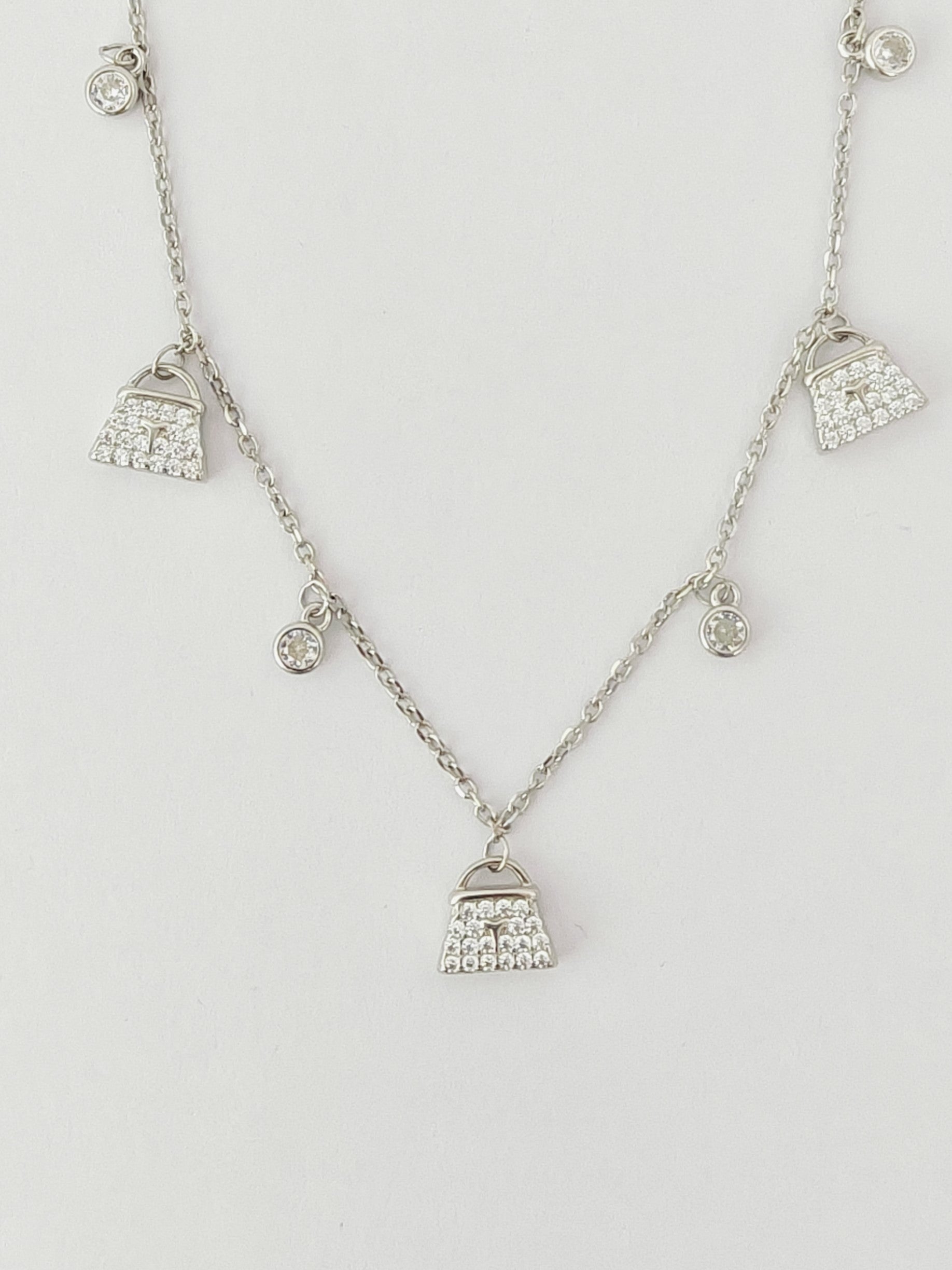 Silver necklace with small bag pendants on a light gray background