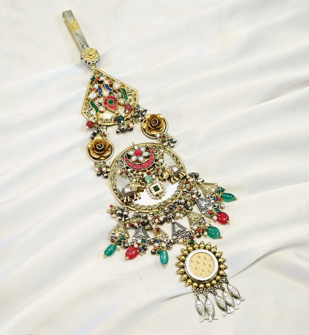 Decorative necklace with gold and multicolor stones on a white fabric background