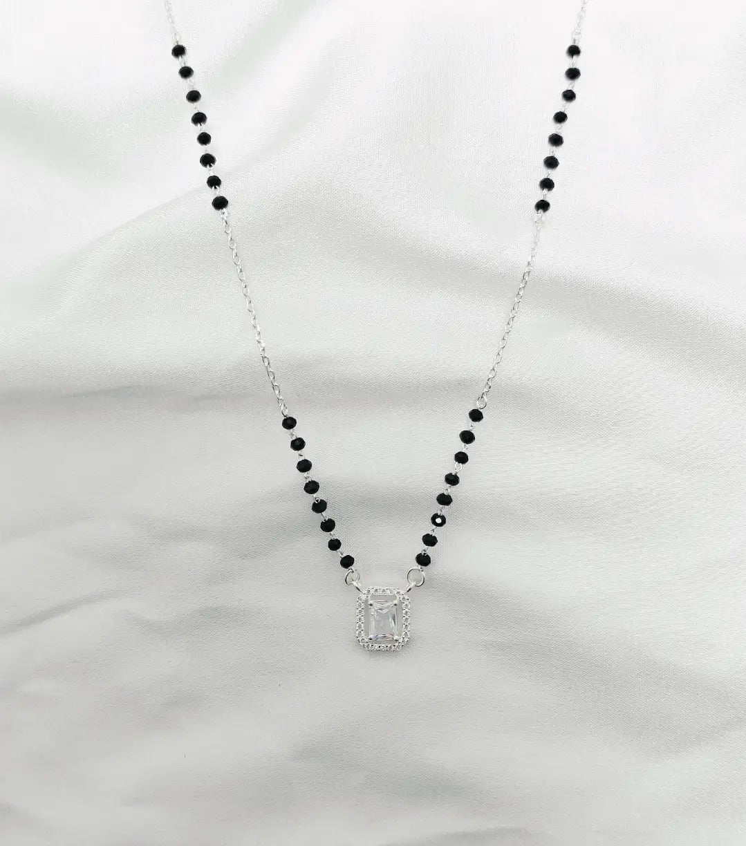Necklace with black beads and a silver pendant on a white background