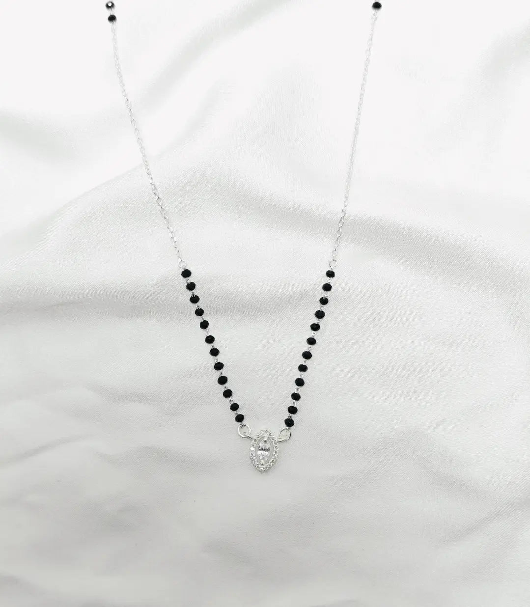 Necklace with black beads and a silver heart pendant on a white fabric background