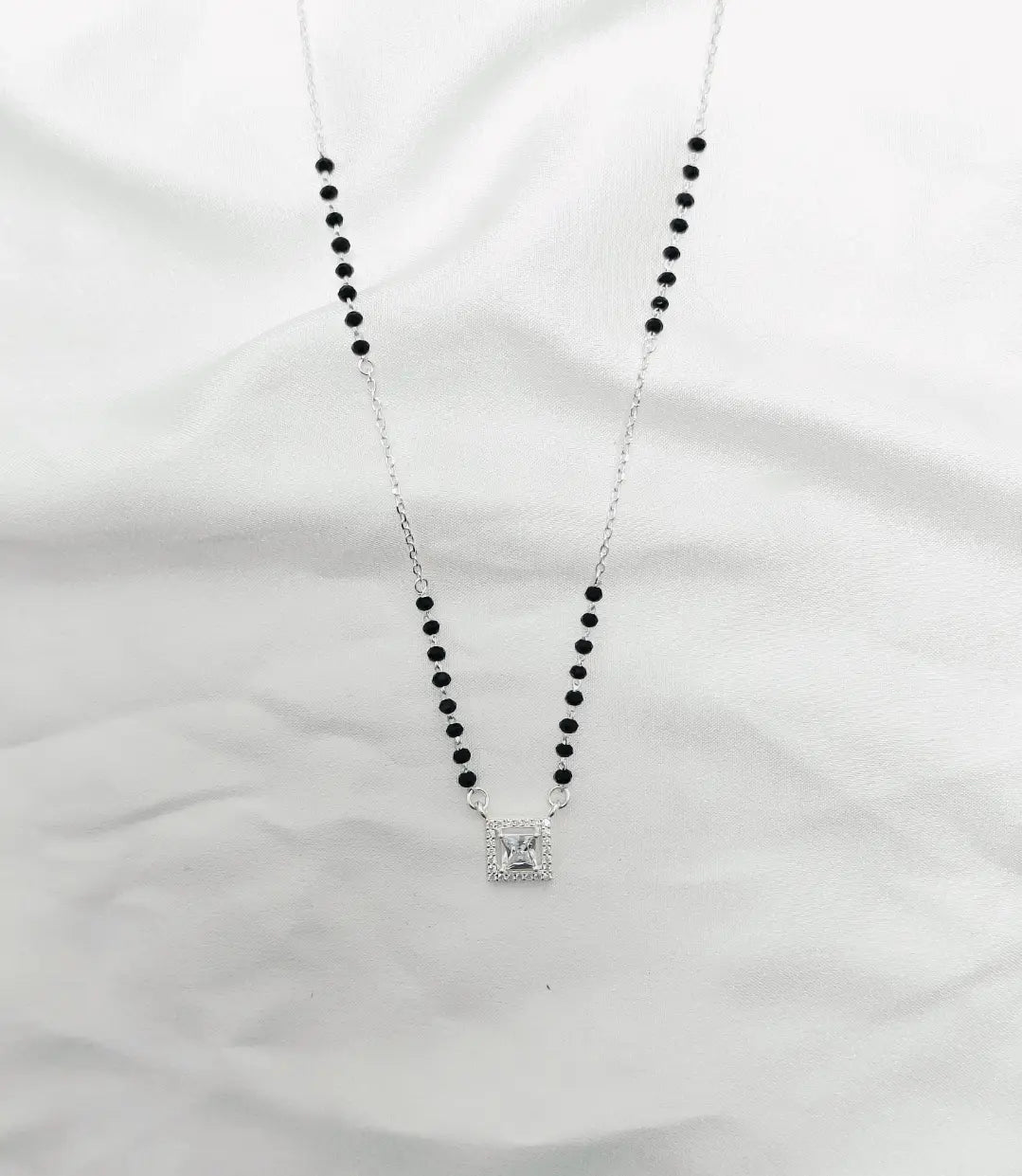 Necklace with black beads and a silver pendant on a white fabric background