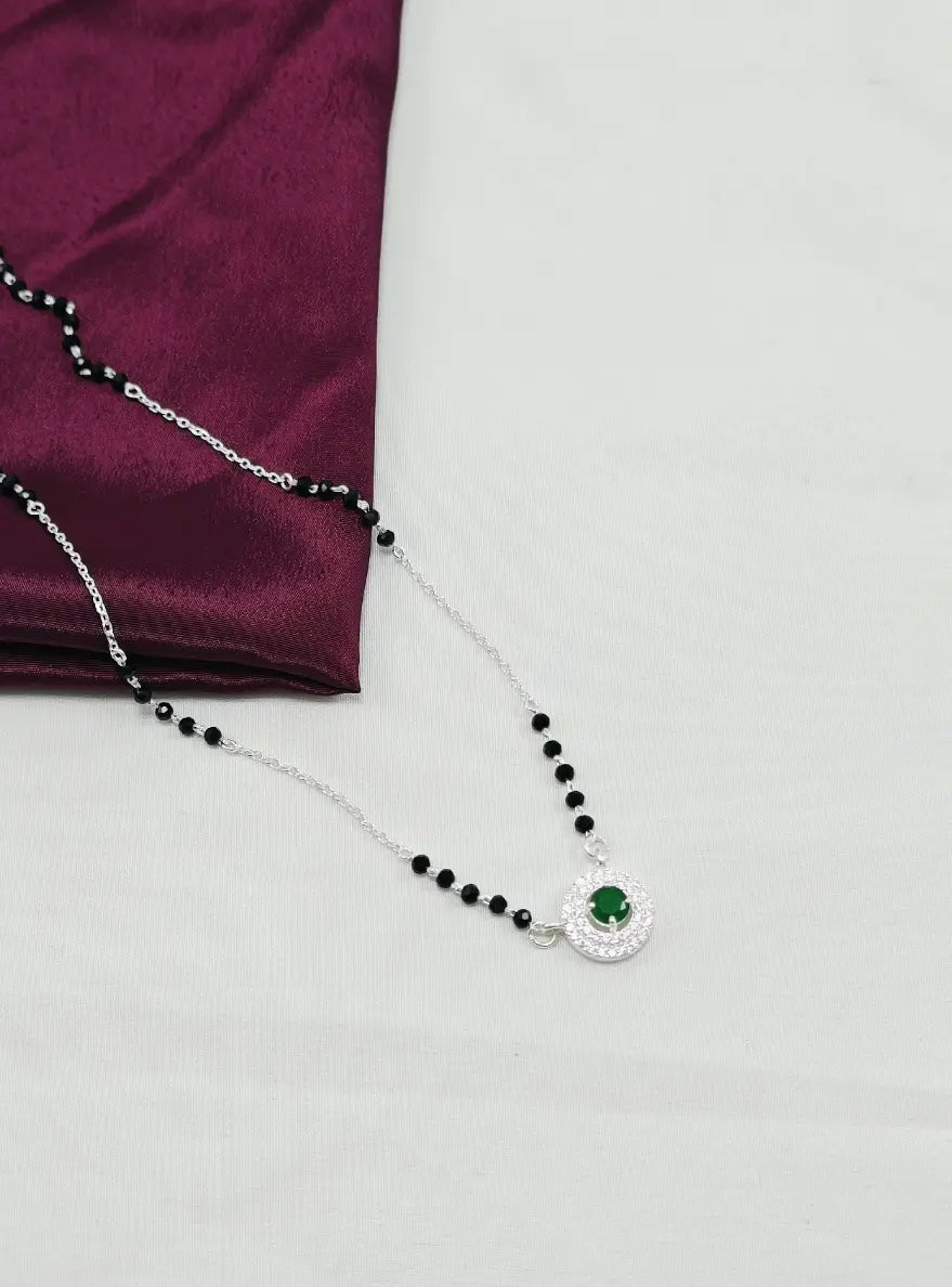 Necklace with black beads and a green gemstone on a white background