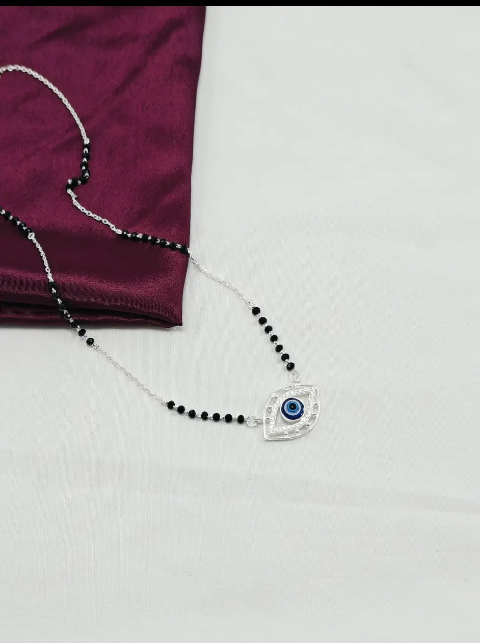 Necklace with black beads and an eye-shaped pendant on a purple fabric background