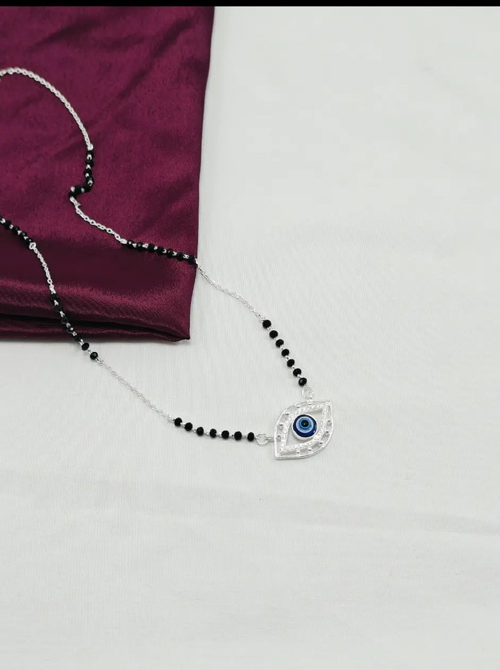 Necklace with black beads and an eye-shaped pendant on a purple fabric background