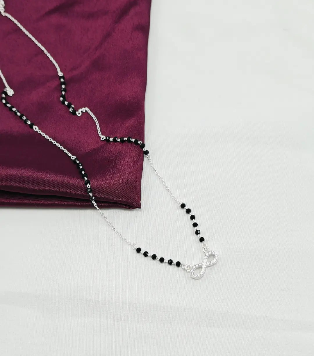 Black beaded necklace on a silver chain draped over a purple fabric on a white background