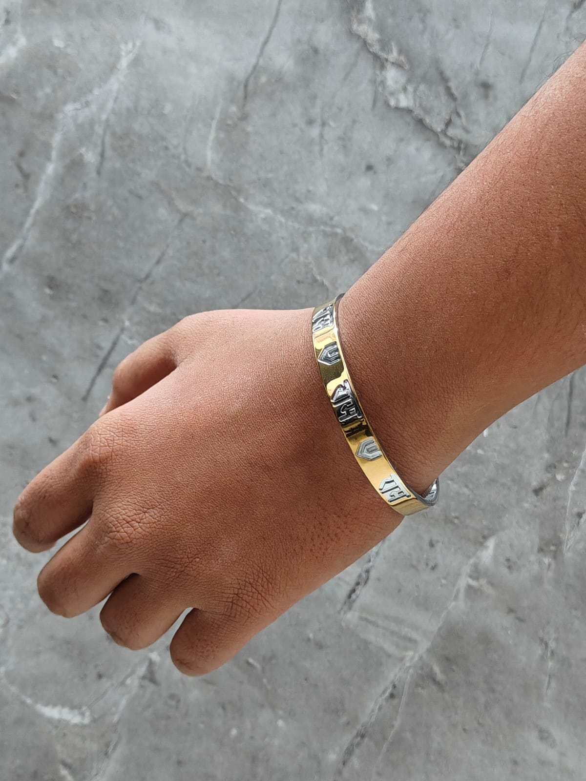Hand wearing a gold bracelet on a gray marble surface