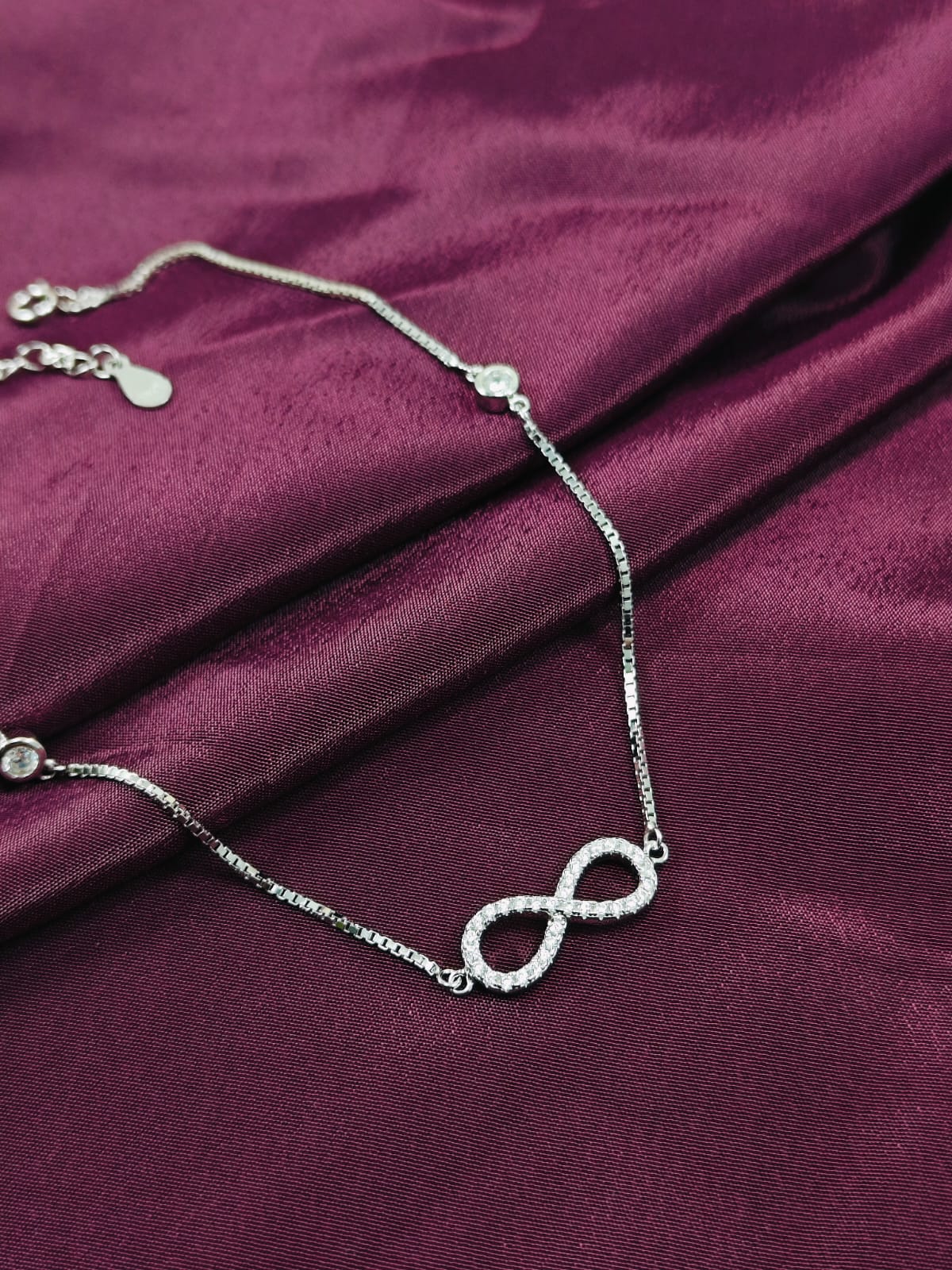 Silver infinity necklace on a burgundy fabric background
