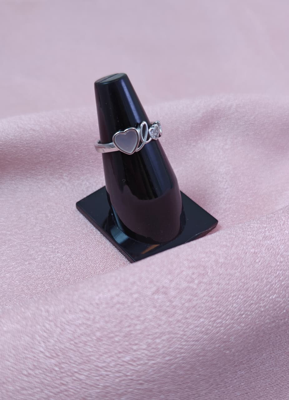 Silver ring with heart design on a black stand against a pink fabric background