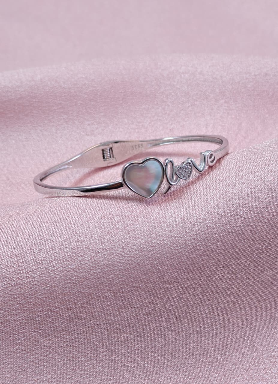 Silver bracelet with heart-shaped charm on a pink background